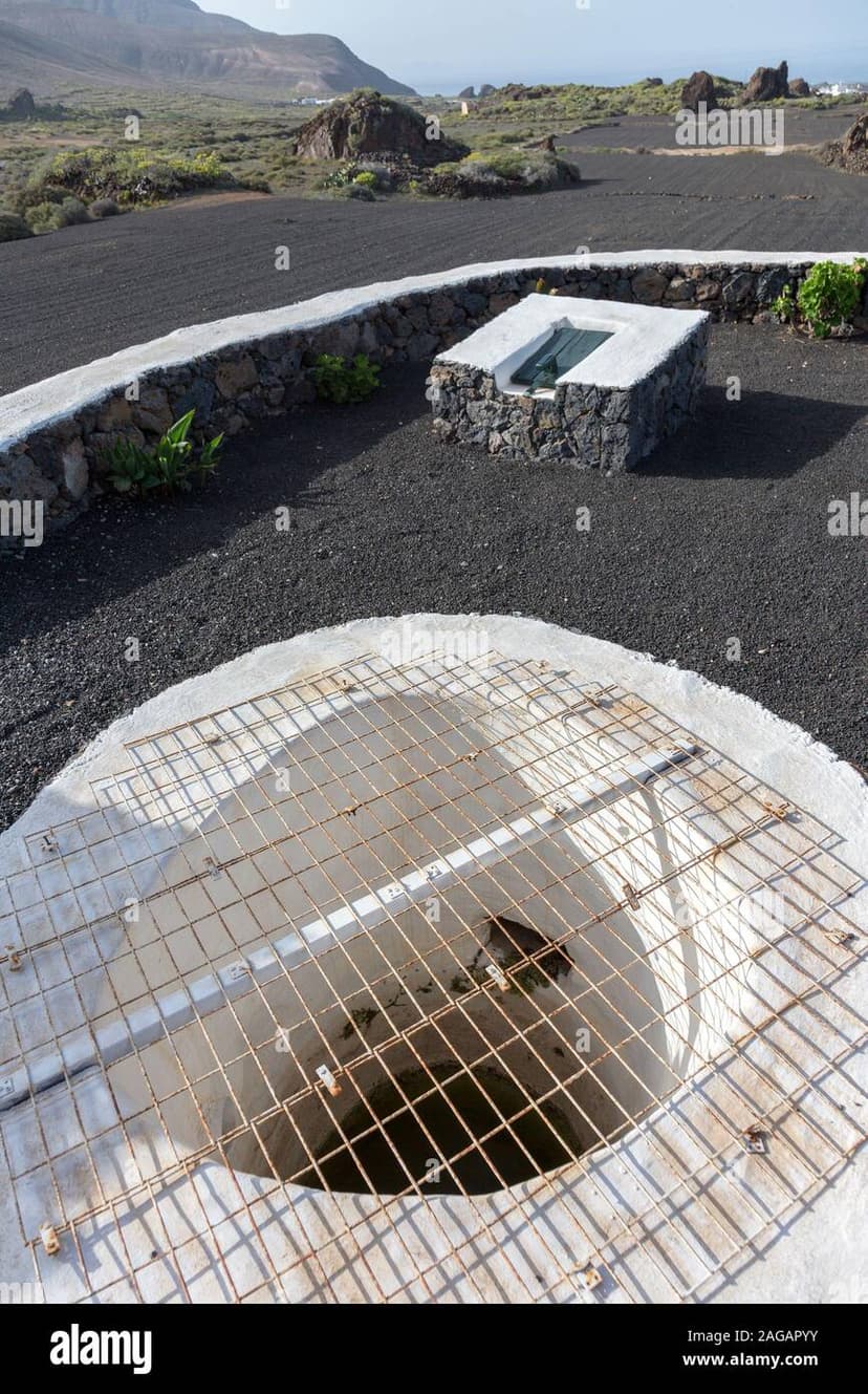 Aljibe canario tradicional mostrando el acceso al tanque subterr\u00e1neo rodeado de suelo volc\u00e1nico en Lanzarote